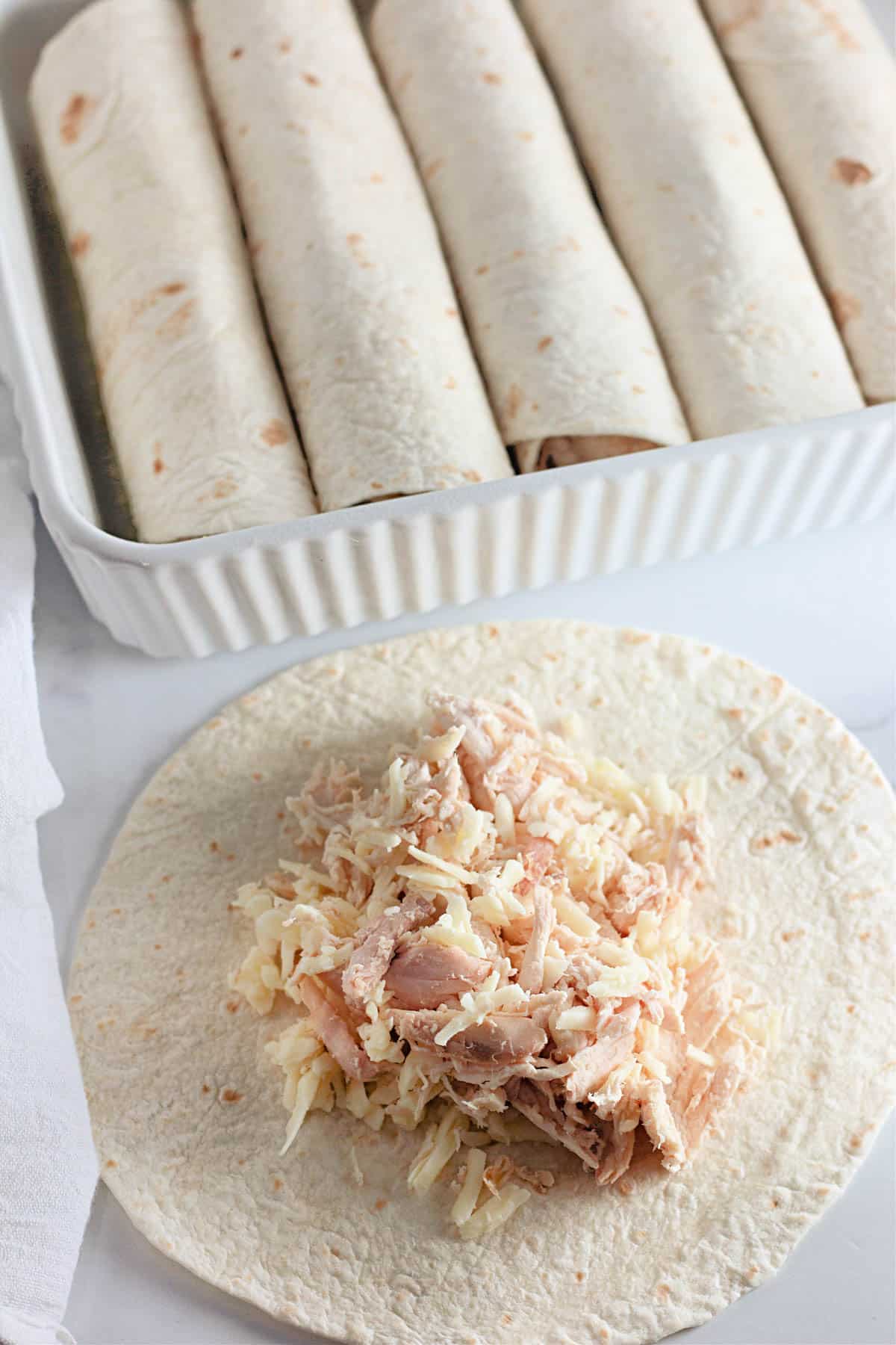 Tortilla with shredded chicken and cheese; rolled tortillas in a baking dish nearby.