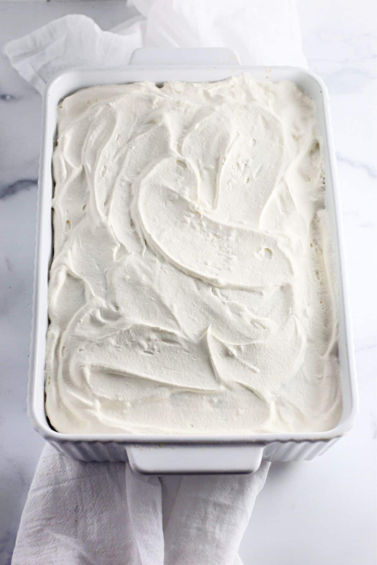 A white rectangular dish filled with dessert topped with a thick layer of whipped cream.