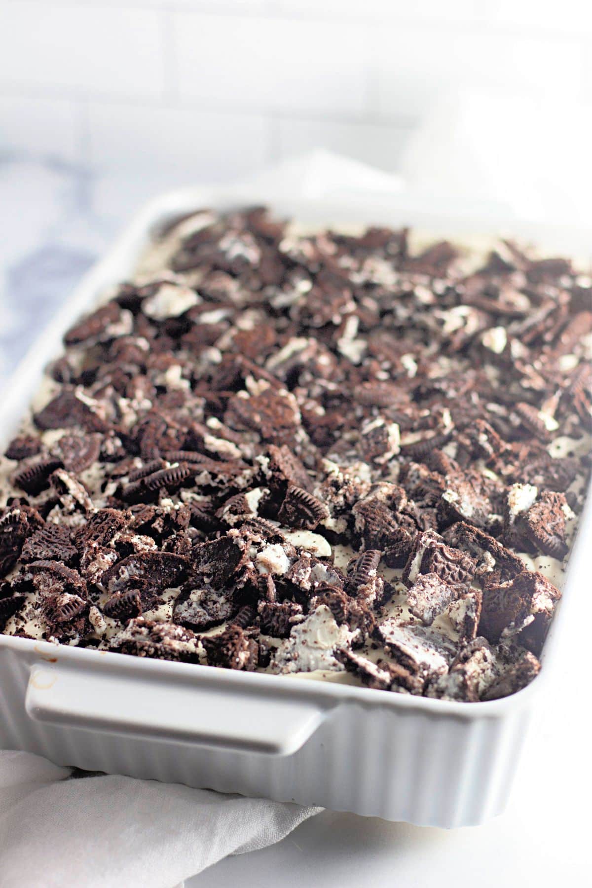 A white baking dish filled with dessert topped with crushed chocolate sandwich cookies.