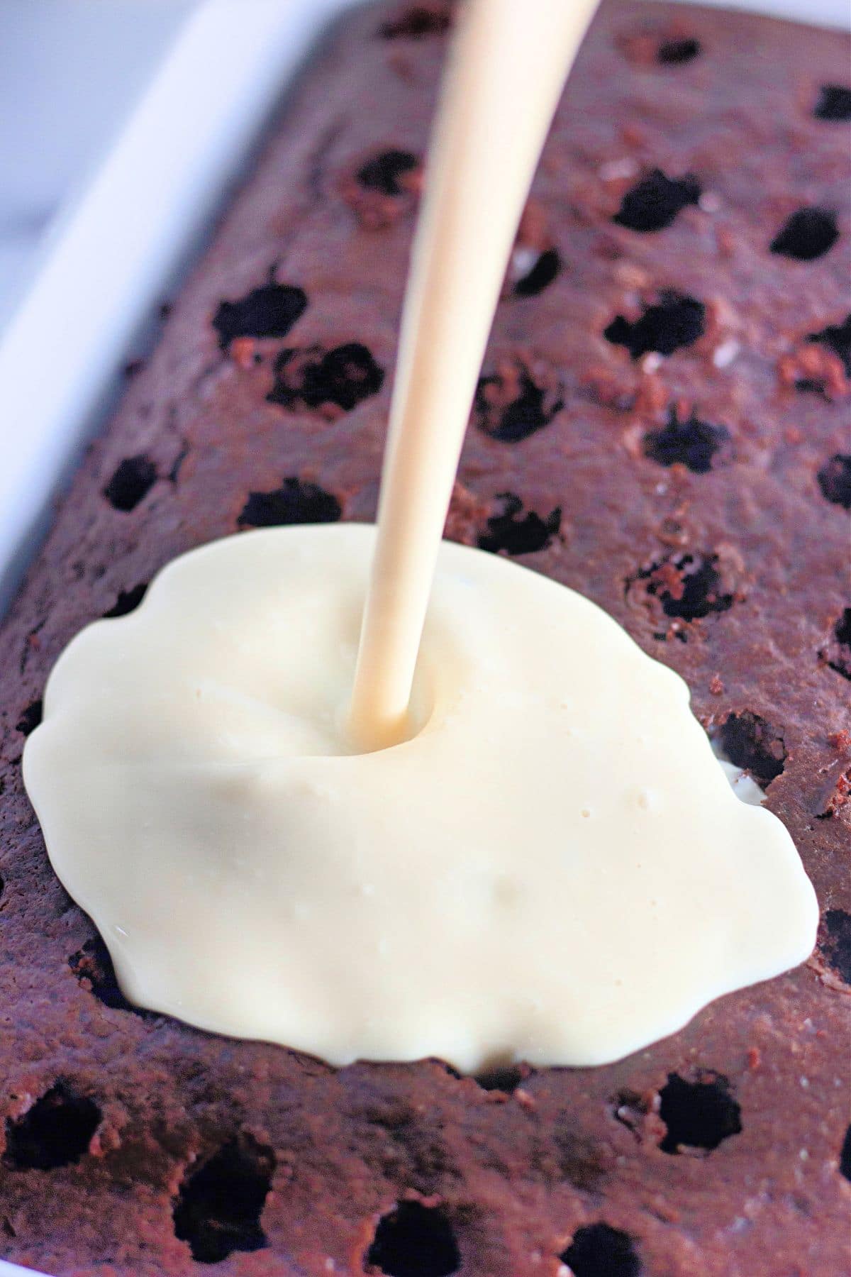 Cream being poured over a chocolate cake with holes on top.