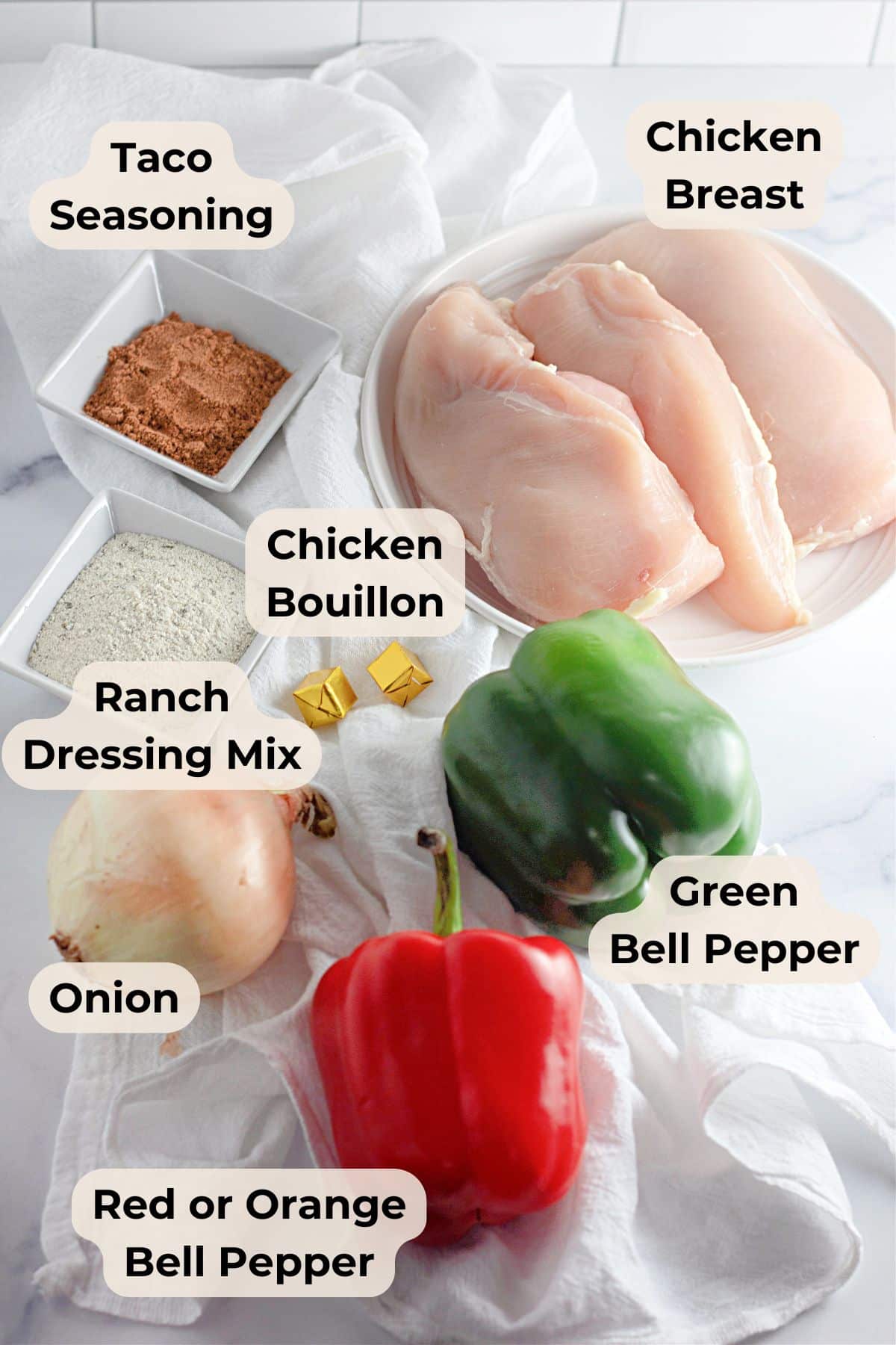 Chicken breasts, taco seasoning, chicken bouillon, ranch mix, onion, green and red bell peppers on a white cloth.