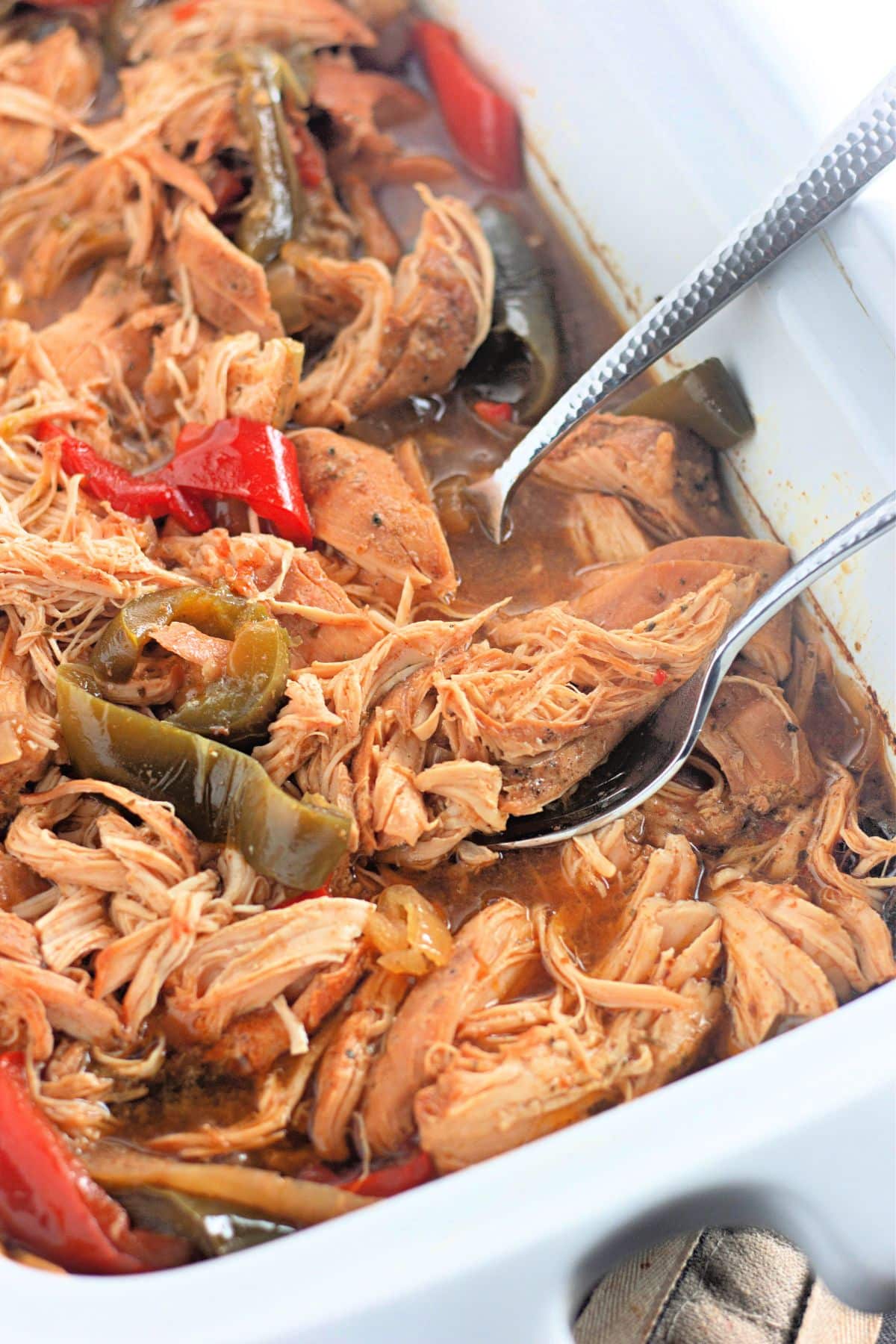 Shredded chicken with bell peppers in a savory sauce, served in a white casserole dish with a serving spoon.