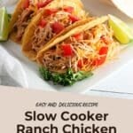 Three chicken tacos with shredded cheese and diced tomatoes, garnished with lime slices, on a white plate.