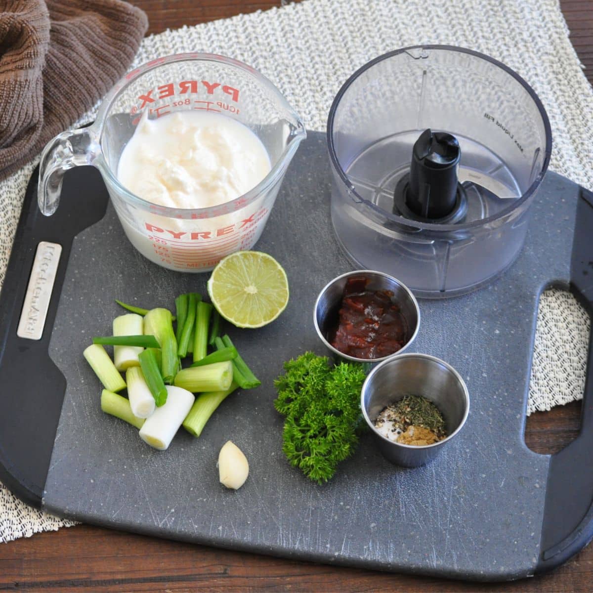 Chopped green onions, parsley, garlic, lime, seasonings, mayo, and chipotle peppers on a cutting board.