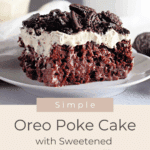 A slice of Oreo Poke Cake topped with whipped cream and crushed Oreos sits on a white plate, perfect for satisfying your sweet tooth.