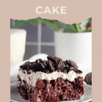 A slice of Oreo Poke Cake with cream and Oreo pieces on top, served on a white plate.