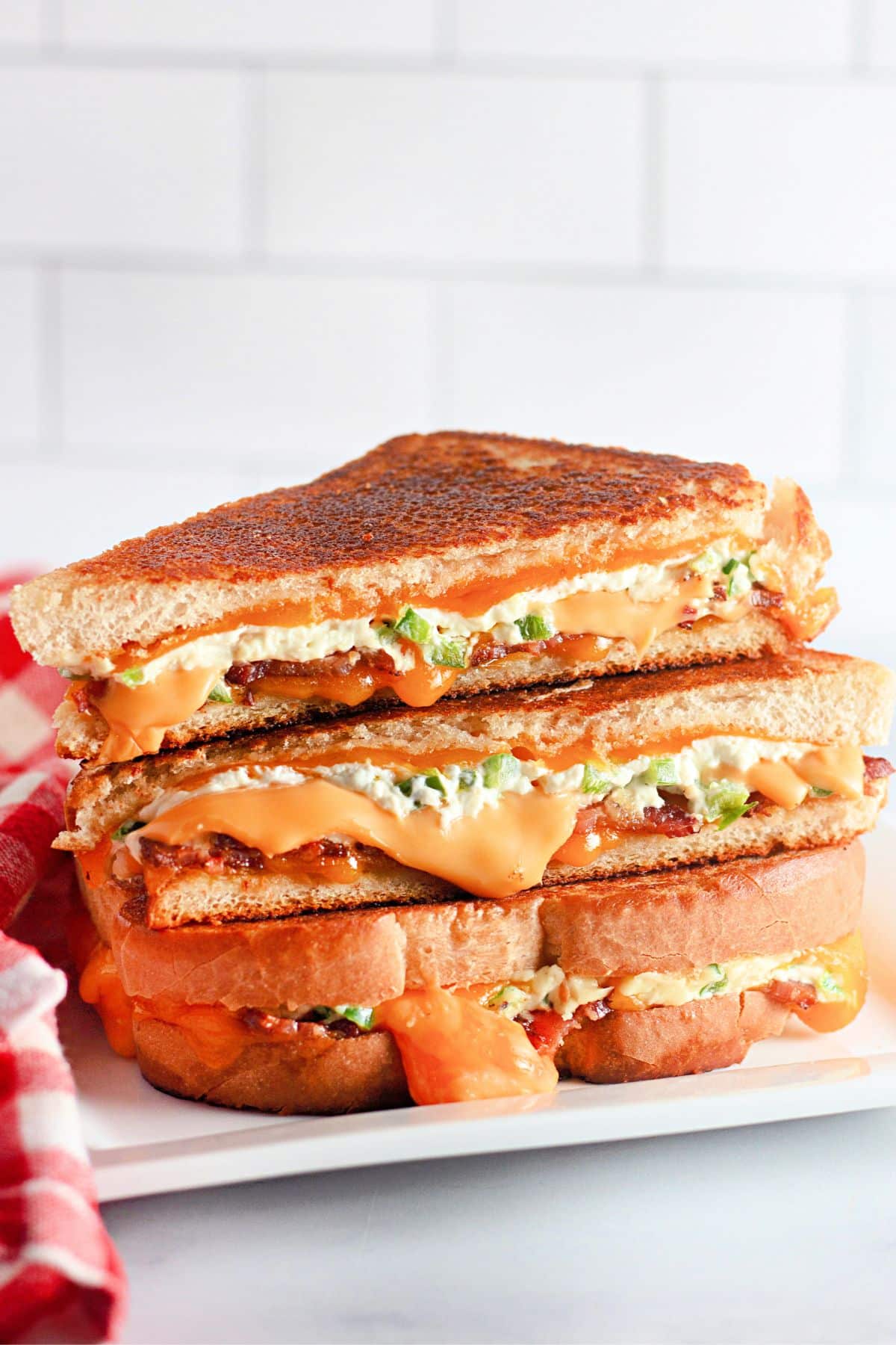 Grilled cheese sandwiches stacked on a plate, filled with melted cheese and green peppers.
