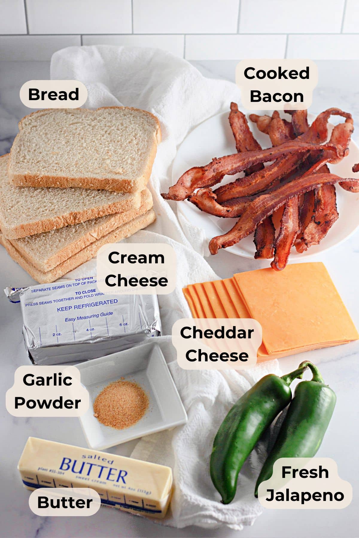 Ingredients for a sandwich: bread, cooked bacon, cream cheese, cheddar, garlic powder, butter, jalapeño.