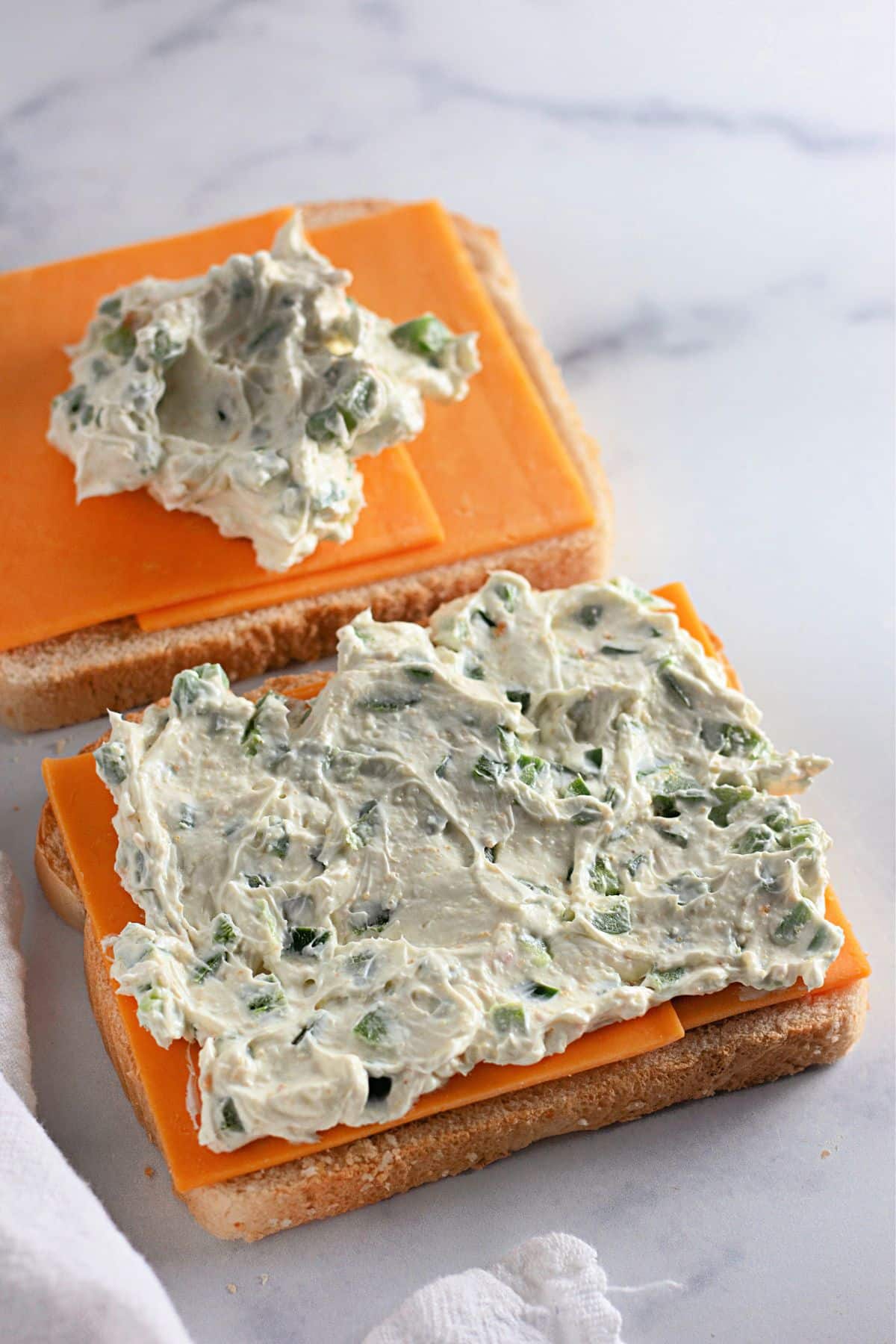 Two slices of bread with cheddar cheese and a layer of jalapeno cream cheese spread on top.