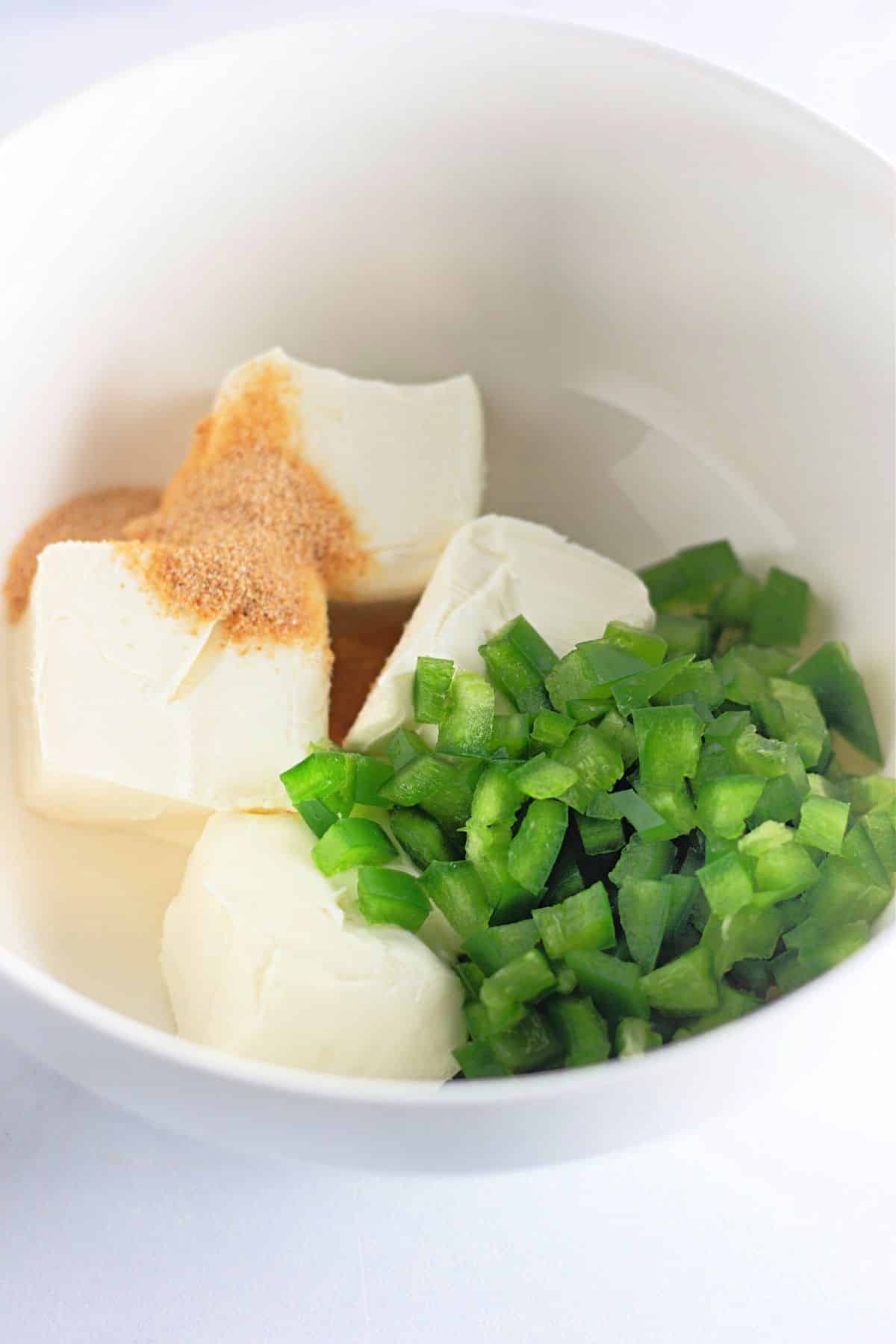 Cream cheese, chopped jalapeno, and garlic powder in a white mixing bowl.