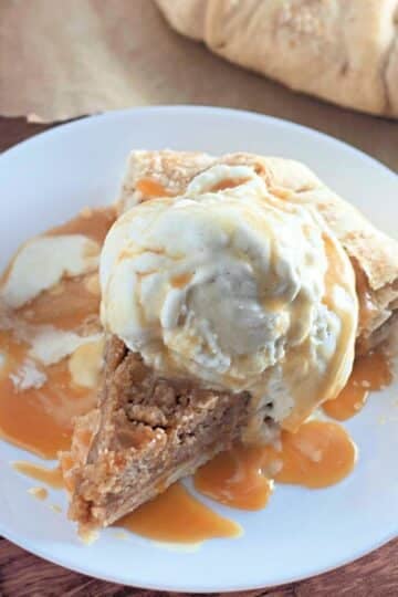A slice of pie topped with vanilla ice cream and caramel sauce on a white plate.