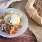 Slice of apple galette with ice cream and caramel sauce on a plate, next to a larger pie on parchment paper.
