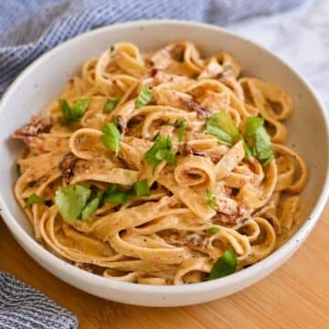 A bowl of creamy fettuccine pasta garnished with fresh parsley on a wooden surface.