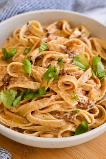 A bowl of creamy fettuccine pasta garnished with fresh parsley on a wooden surface.