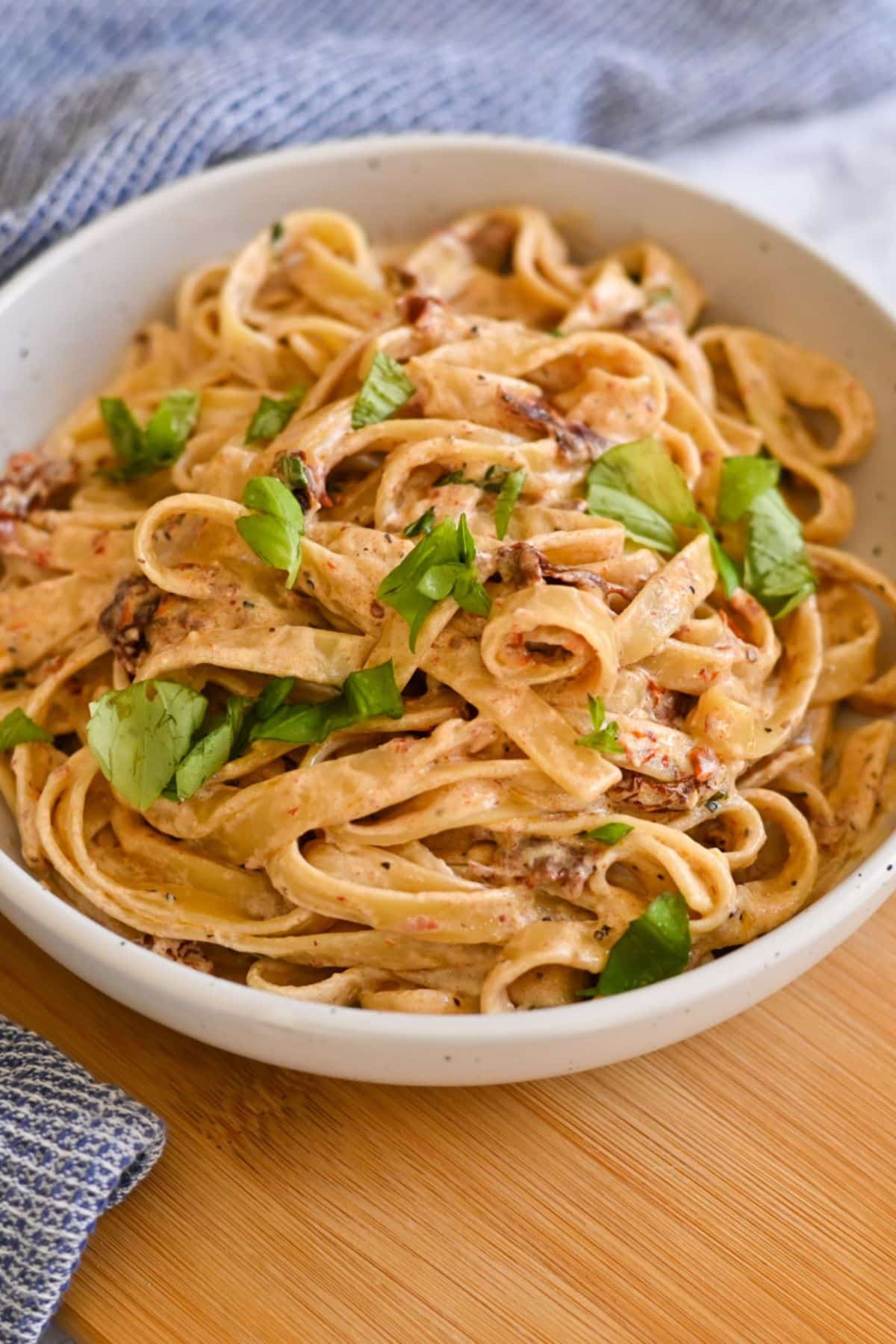 A bowl of creamy fettuccine pasta garnished with fresh basil leaves on a wooden surface.
