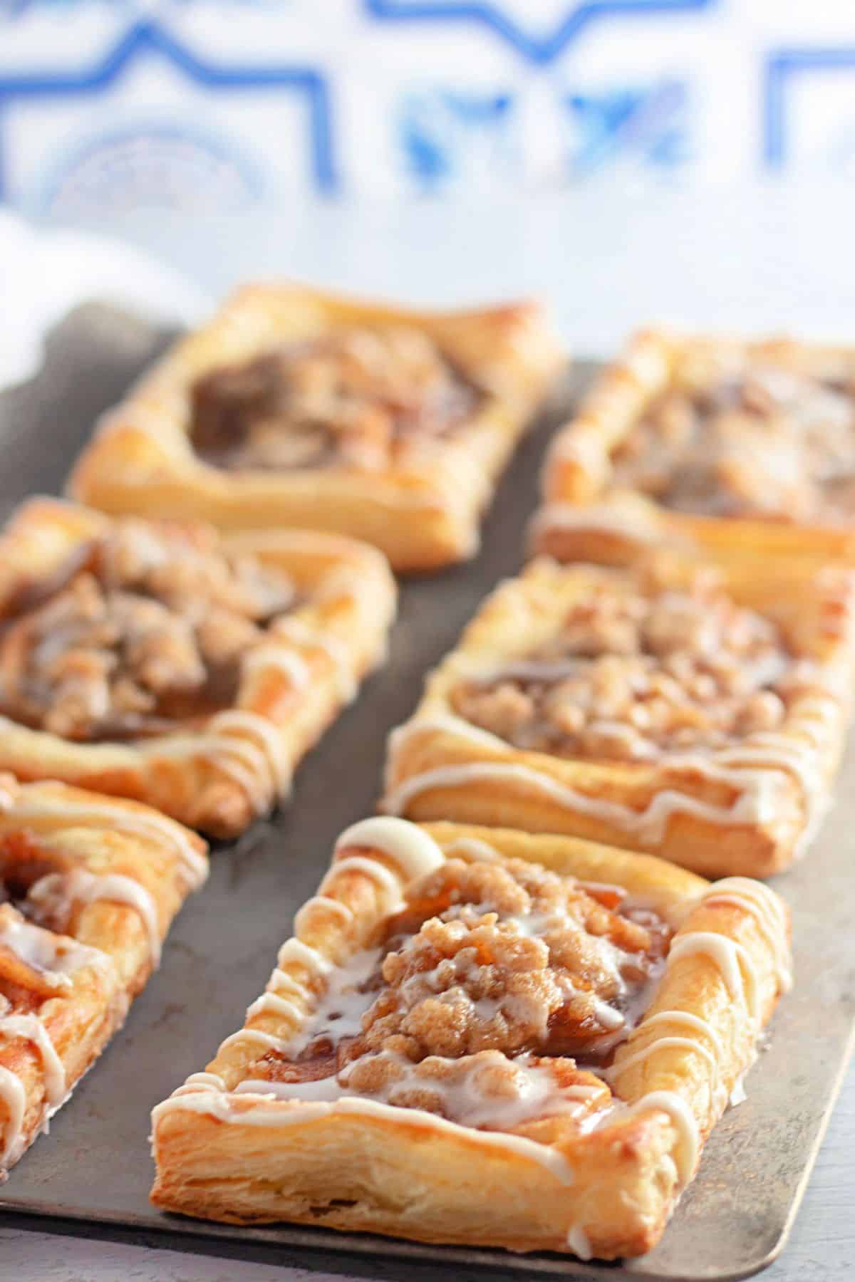 Rectangular puff pastries with crumb topping and white icing, arranged on a baking tray.