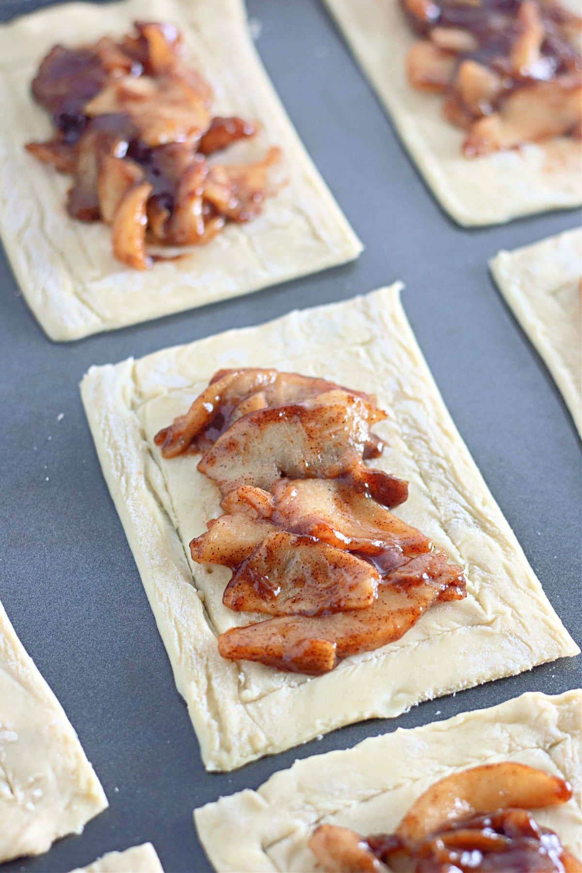 Rectangular pieces of dough topped with cinnamon-spiced apple filling on a baking sheet.