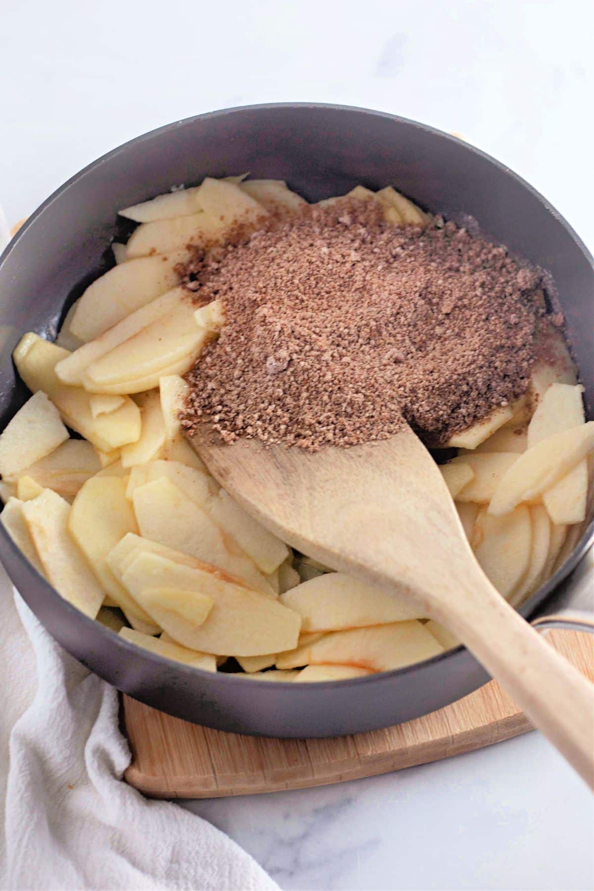 Sliced apples in a pan with brown sugar and spices, stirred with a wooden spoon.