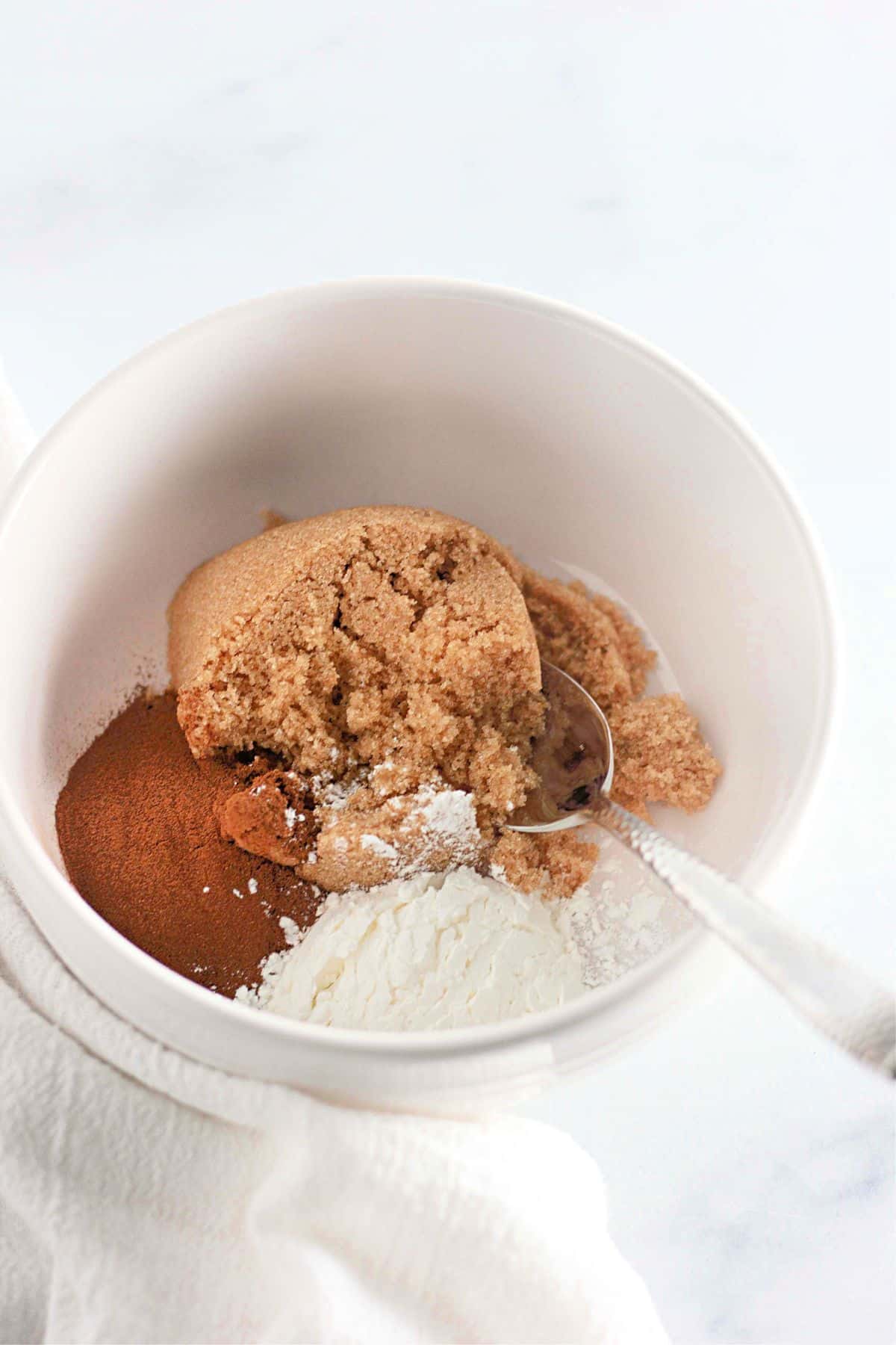 White bowl with brown sugar, cinnamon, and flour, with a silver spoon mixing the ingredients.