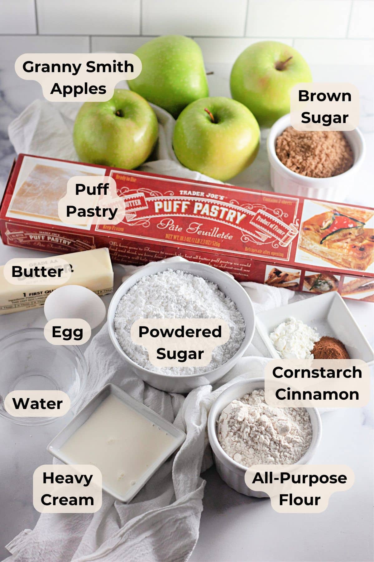 Apple Danish Ingredients Labeled baking ingredients including apples, brown sugar, puff pastry, butter, egg, cream, and flours on a counter.