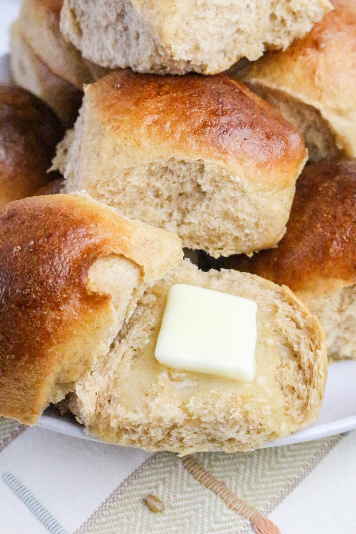 A stack of golden brown bread rolls, one split open with a pat of butter melting on top.