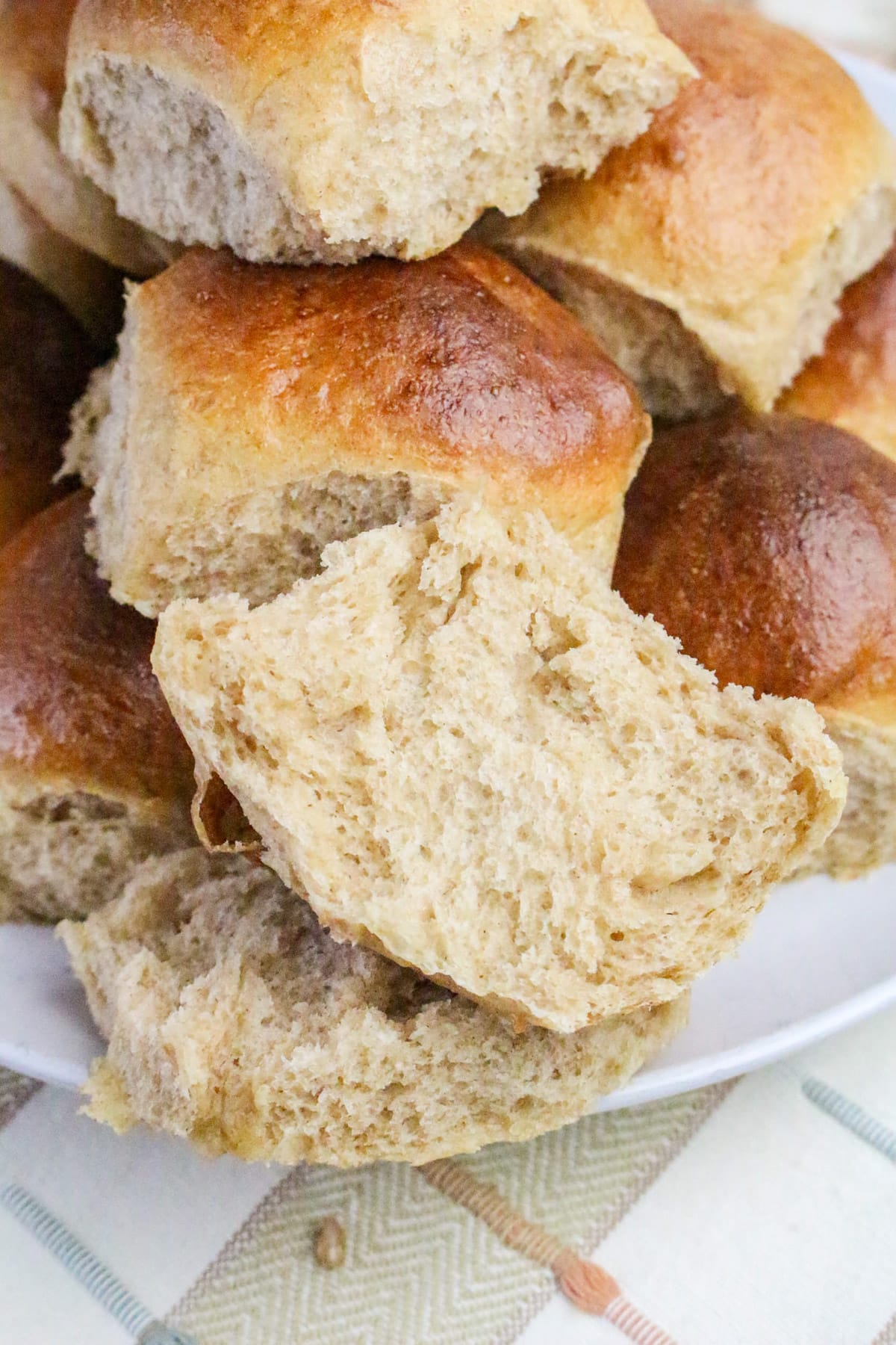A plate of fluffy whole wheat bread rolls, with one roll partially pulled apart to show its soft texture.