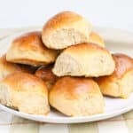 A plate stacked with golden brown, fluffy dinner rolls on a checkered tablecloth.