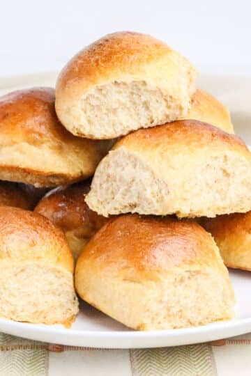 A plate stacked with golden brown, fluffy dinner rolls on a checkered tablecloth.
