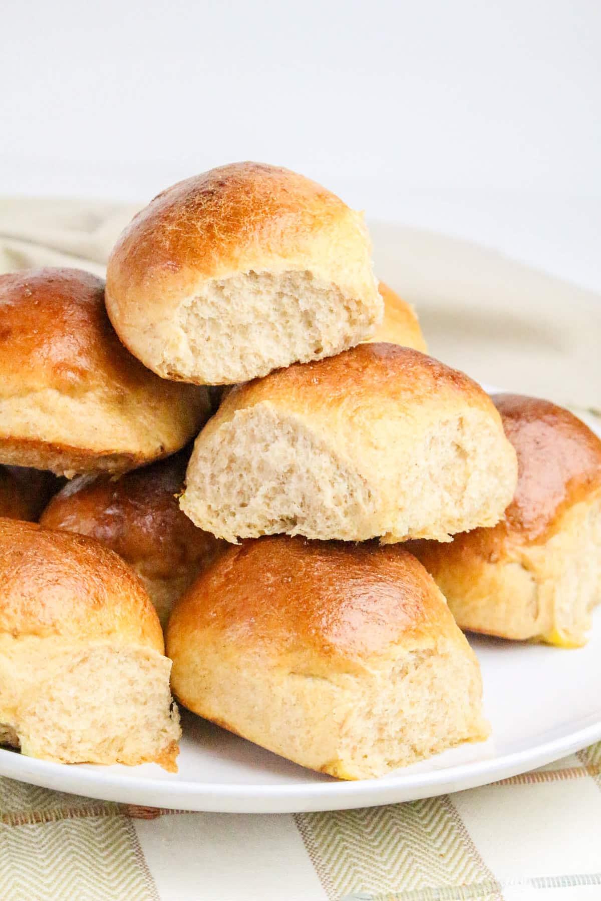 A plate of stacked golden brown dinner rolls with a soft, fluffy texture.