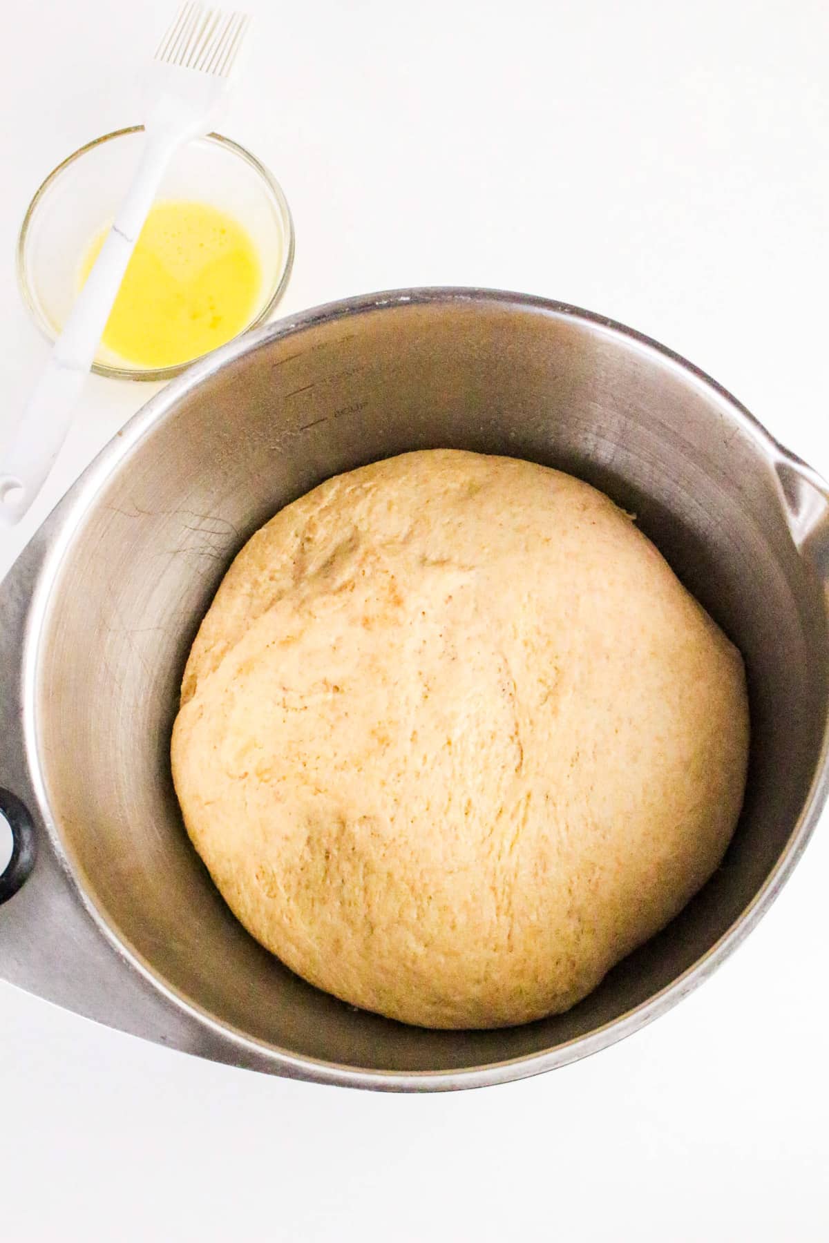 A bowl of risen dough next to a glass bowl of melted butter and a pastry brush on a white surface.