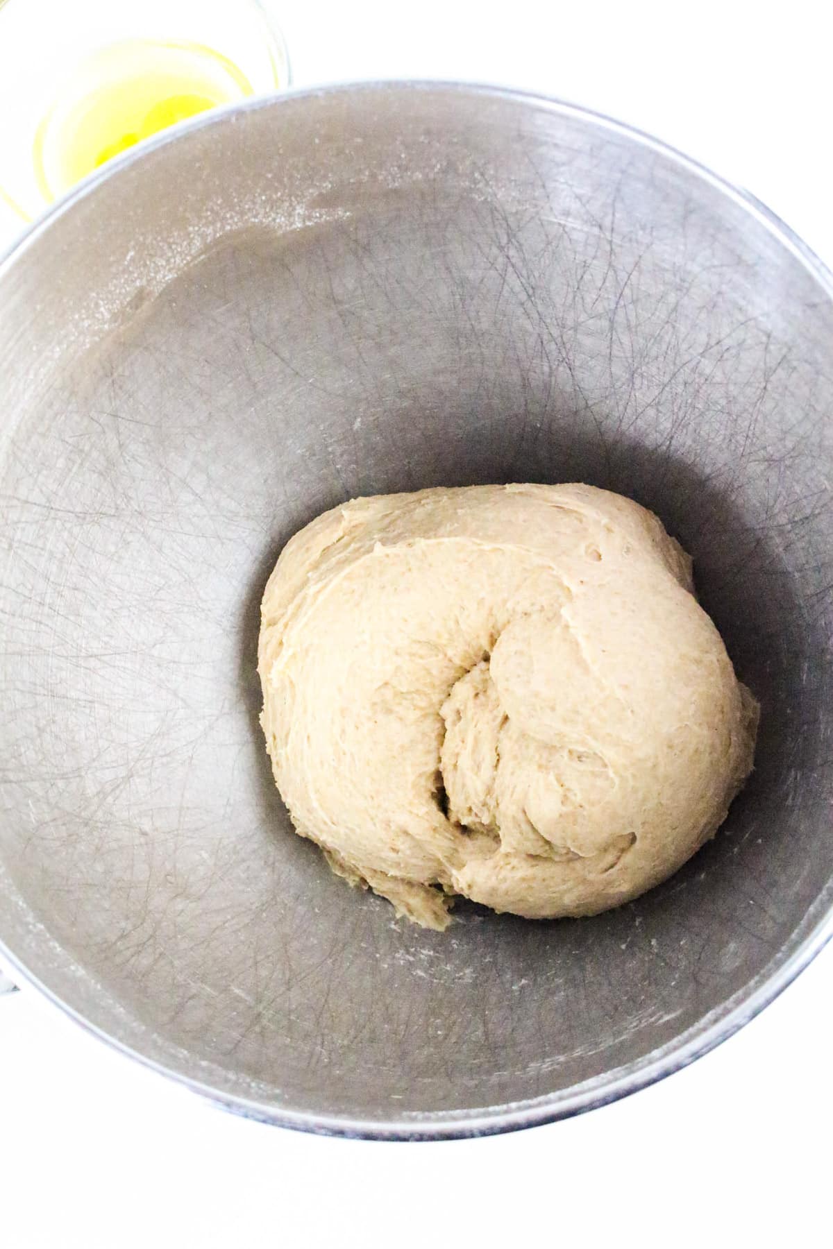 Ball of bread dough in a metal mixing bowl with a small bowl of oil visible in the background.