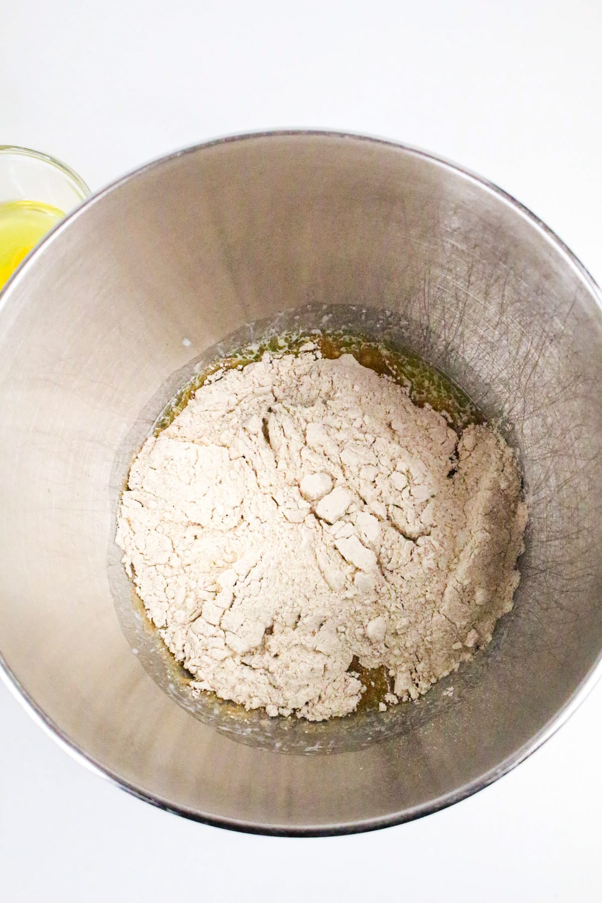 A mixing bowl with flour and wet ingredients, next to a small bowl of melted butter on a white surface.