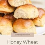 A plate of golden brown Honey Wheat Dinner Rolls stacked on a white dish.