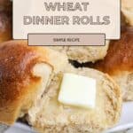 A plate of Honey Wheat Dinner Rolls, one roll open with a pat of butter melting on top.
