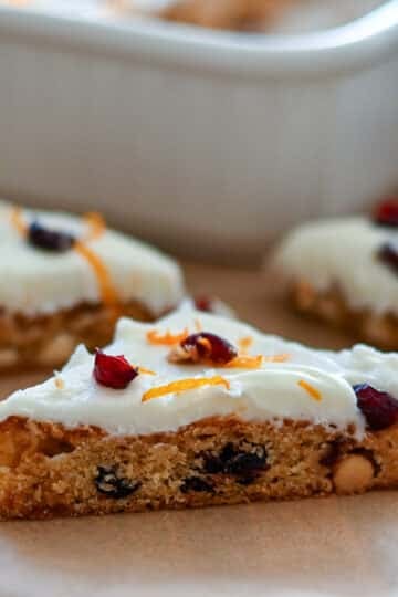 A frosted cranberry and orange cookie bar with white icing and orange zest, cut into a triangle.