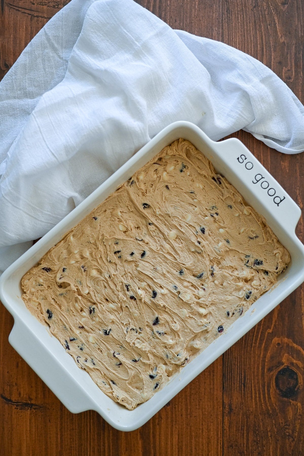 Rectangular baking dish with cookie dough and chocolate chips, on a wooden table with a white cloth.