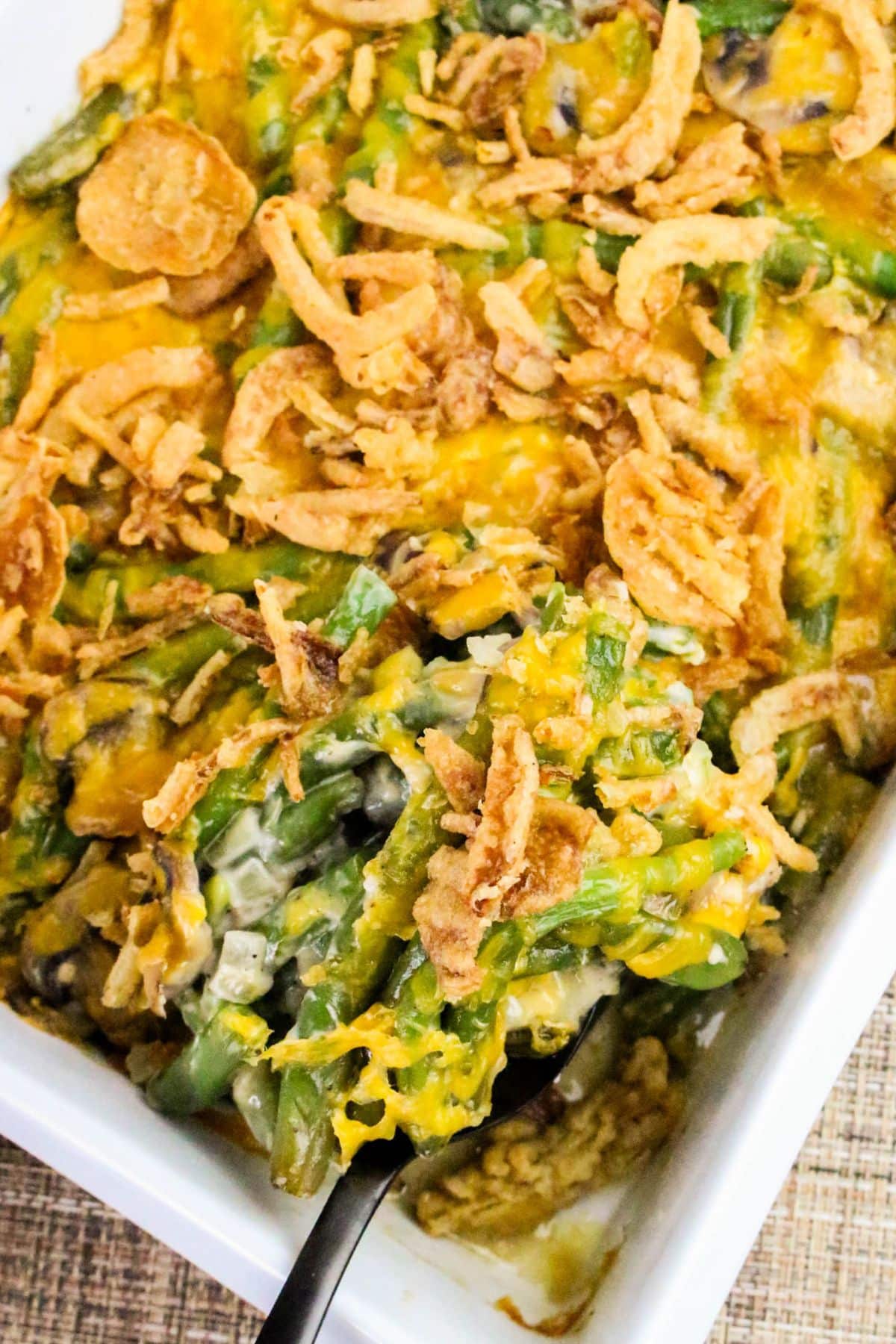 Green bean casserole topped with crispy fried onions in a white baking dish, with a serving spoon scooping some.