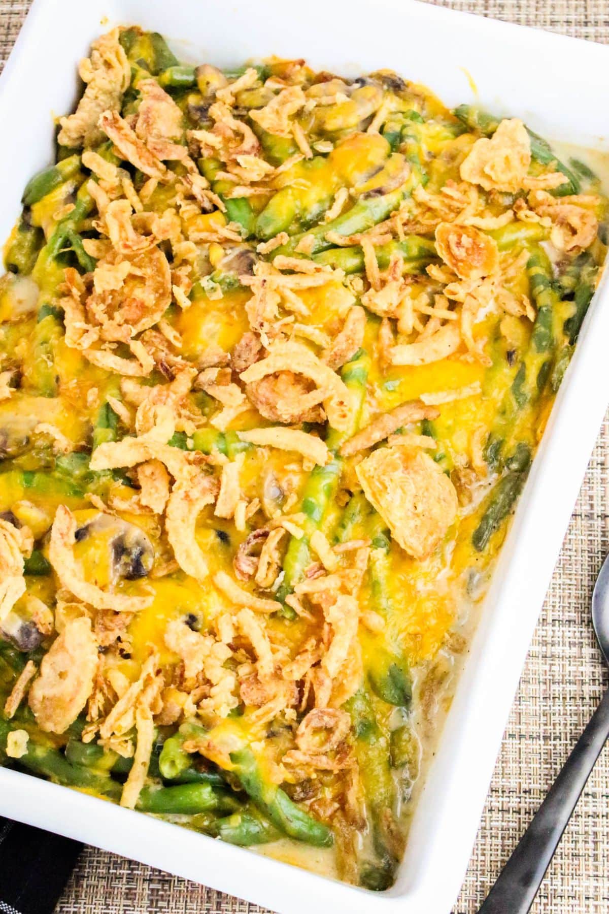 A casserole dish filled with green bean casserole topped with crispy fried onions and melted cheese.