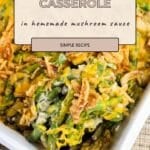 Fresh Green Bean Casserole topped with crispy onions and melted cheese is served in a white baking dish with a serving spoon.