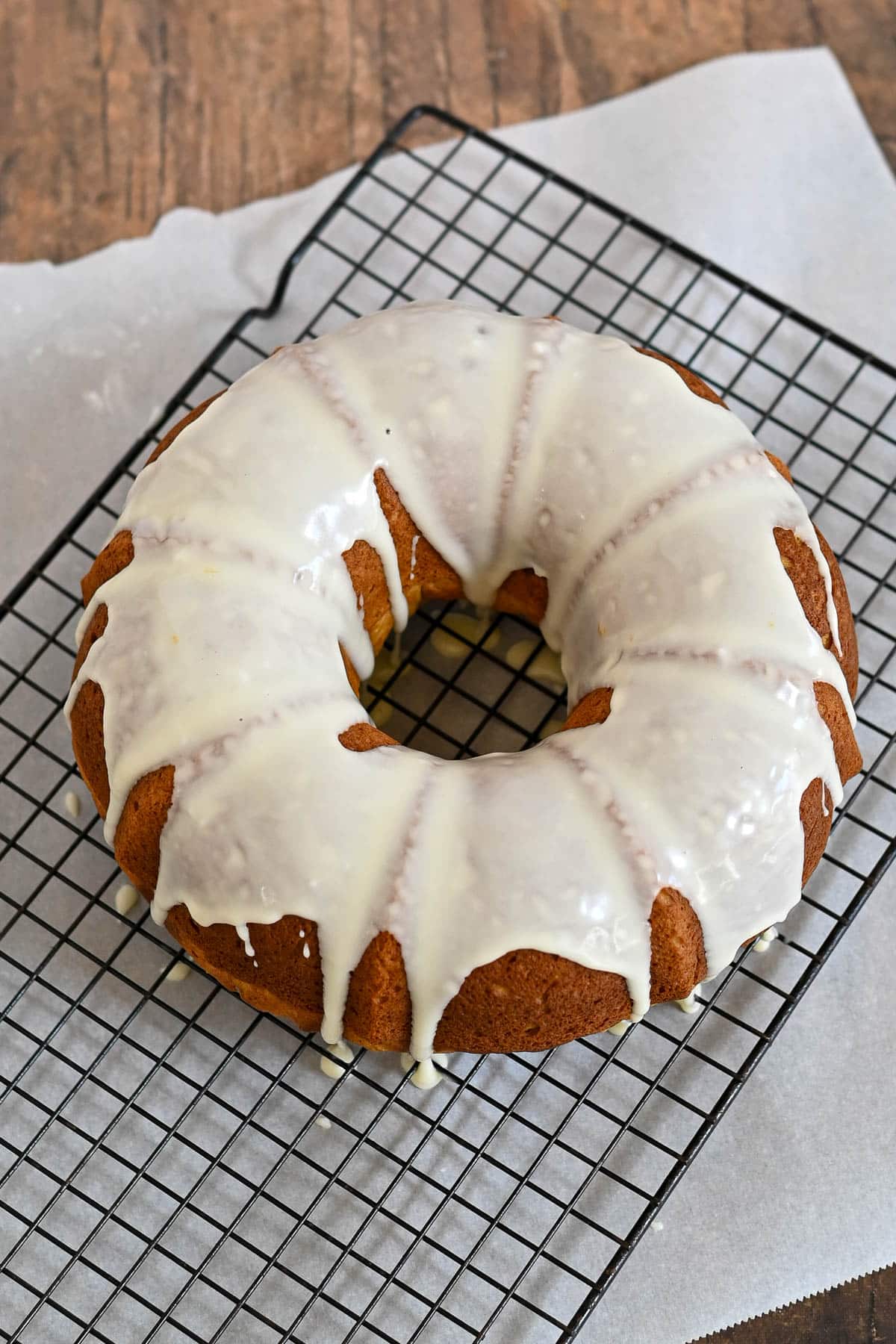 Bundt cake with white icing drizzled on top, cooling on a wire rack lined with parchment paper.