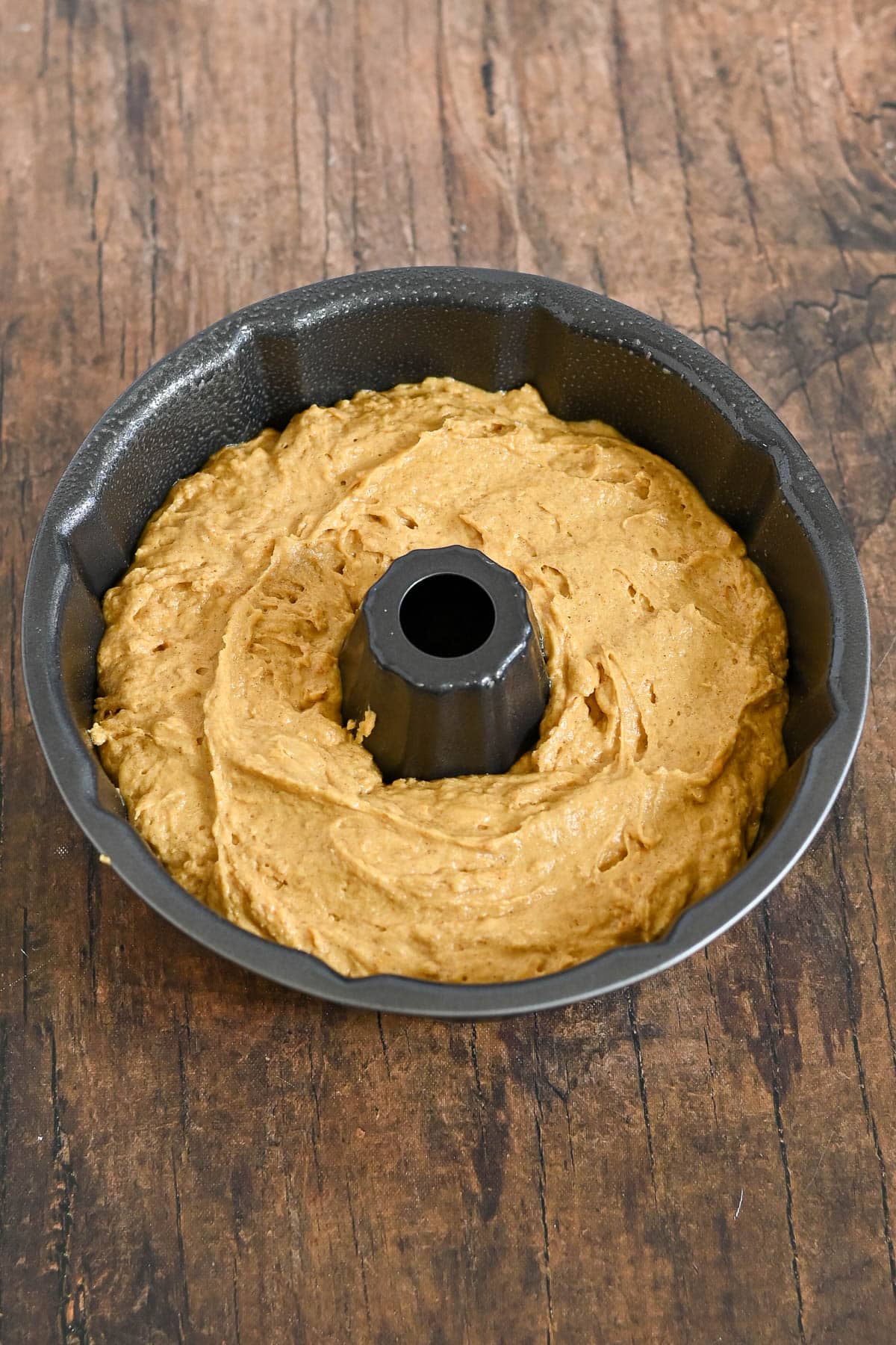 Pumpkin cake batter in a bundt pan on a rustic wooden surface, ready to be baked.