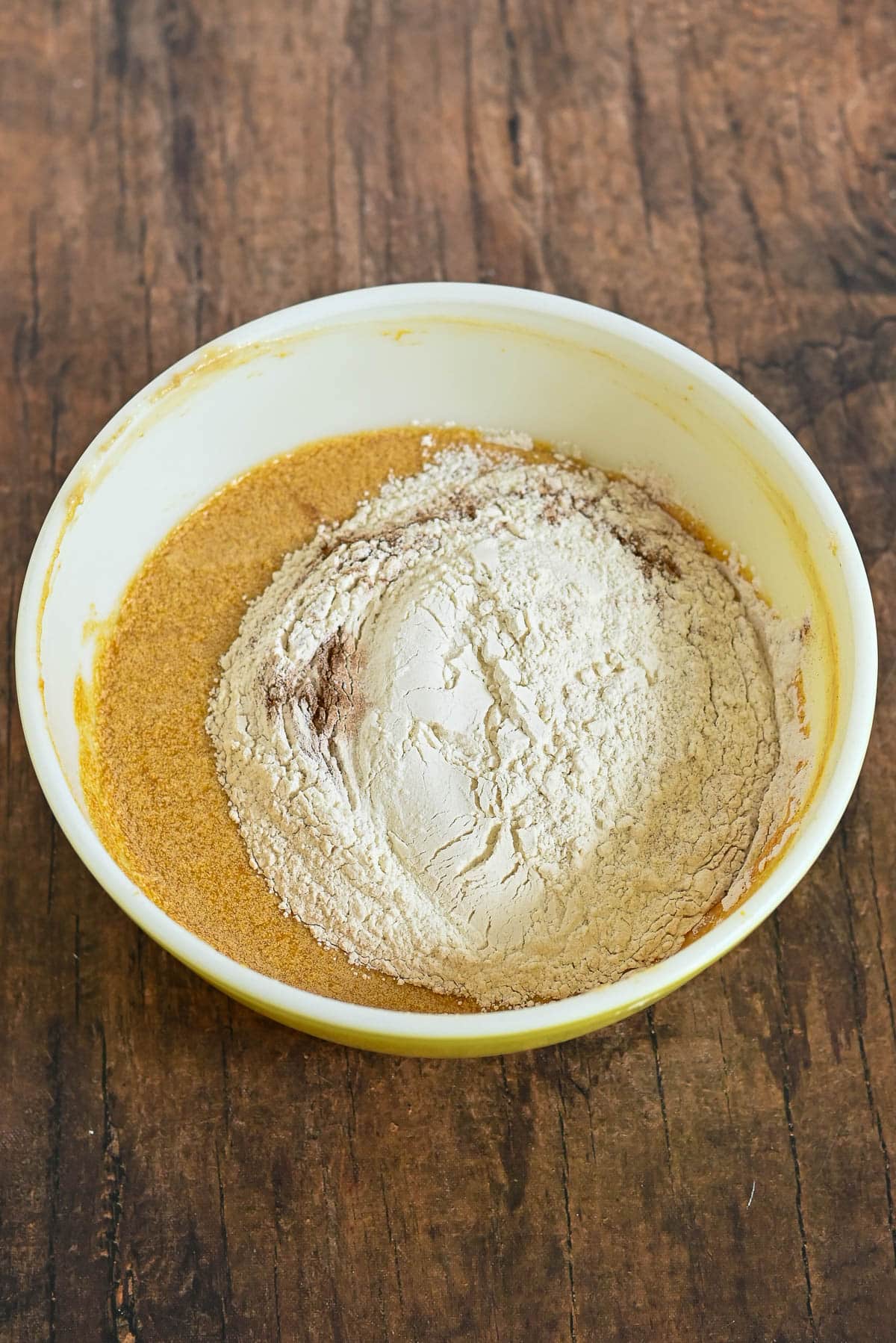 A mixing bowl with flour and wet ingredients on a wooden surface, ready to be mixed.