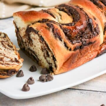 A sliced loaf of chocolate swirl bread on a white plate with chocolate chips beside it.