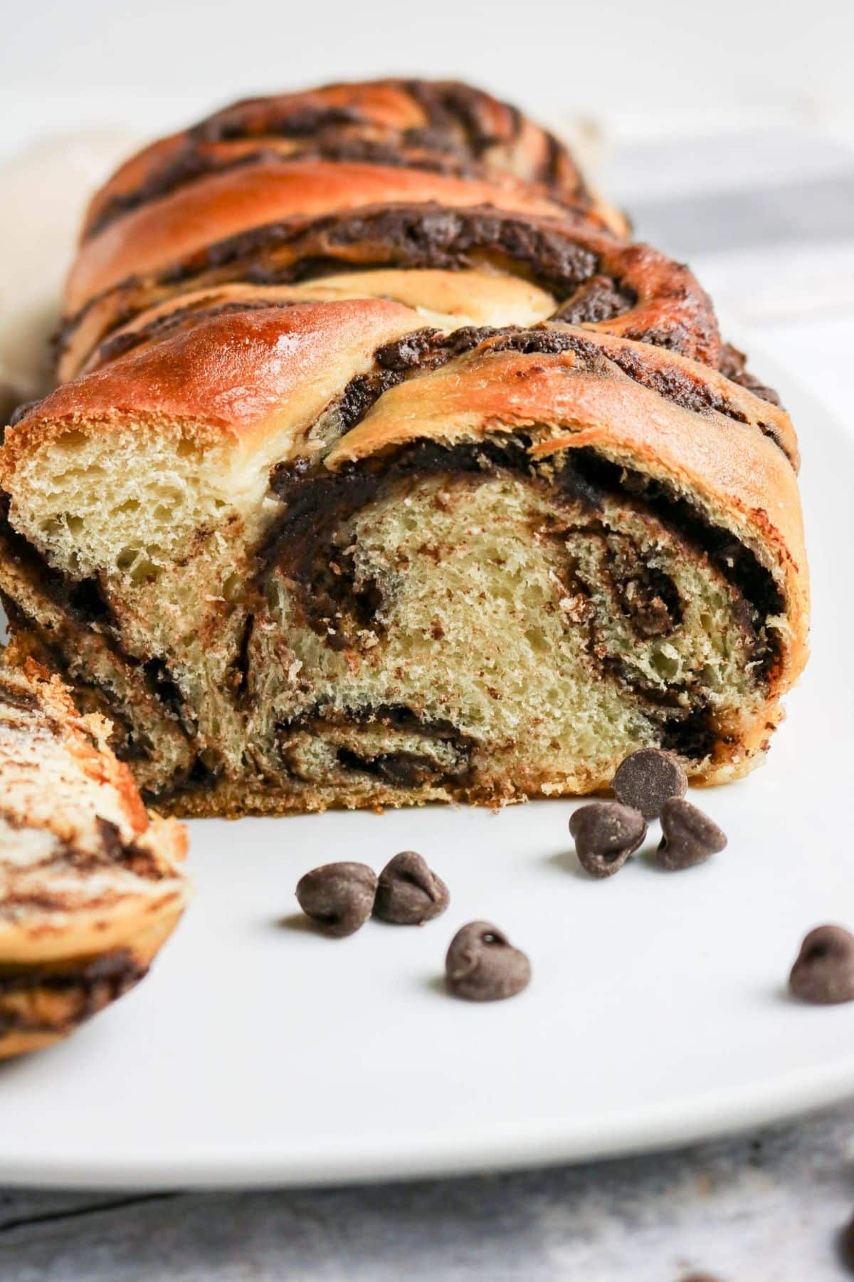 A sliced chocolate babka loaf on a white plate, with chocolate chips scattered nearby.