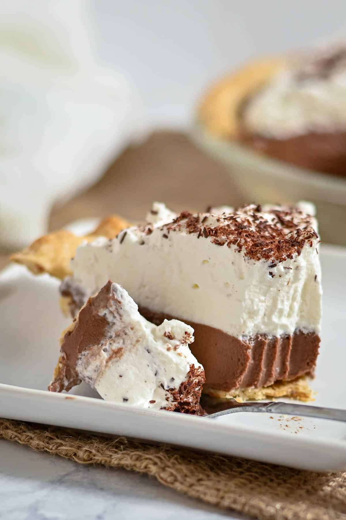 A slice of chocolate cream pie topped with whipped cream and chocolate shavings on a white plate.