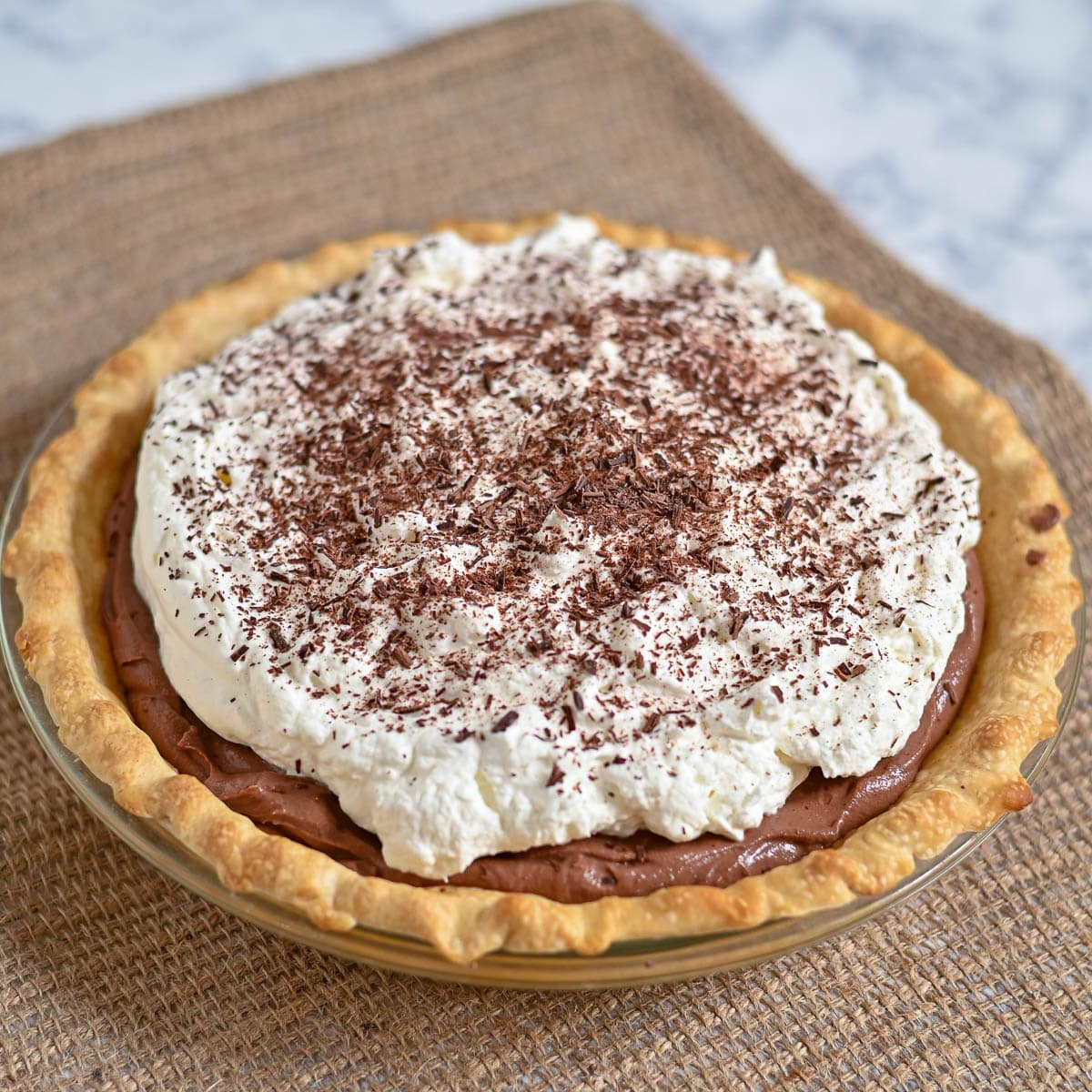Chocolate cream pie topped with whipped cream and chocolate shavings on a burlap placemat.