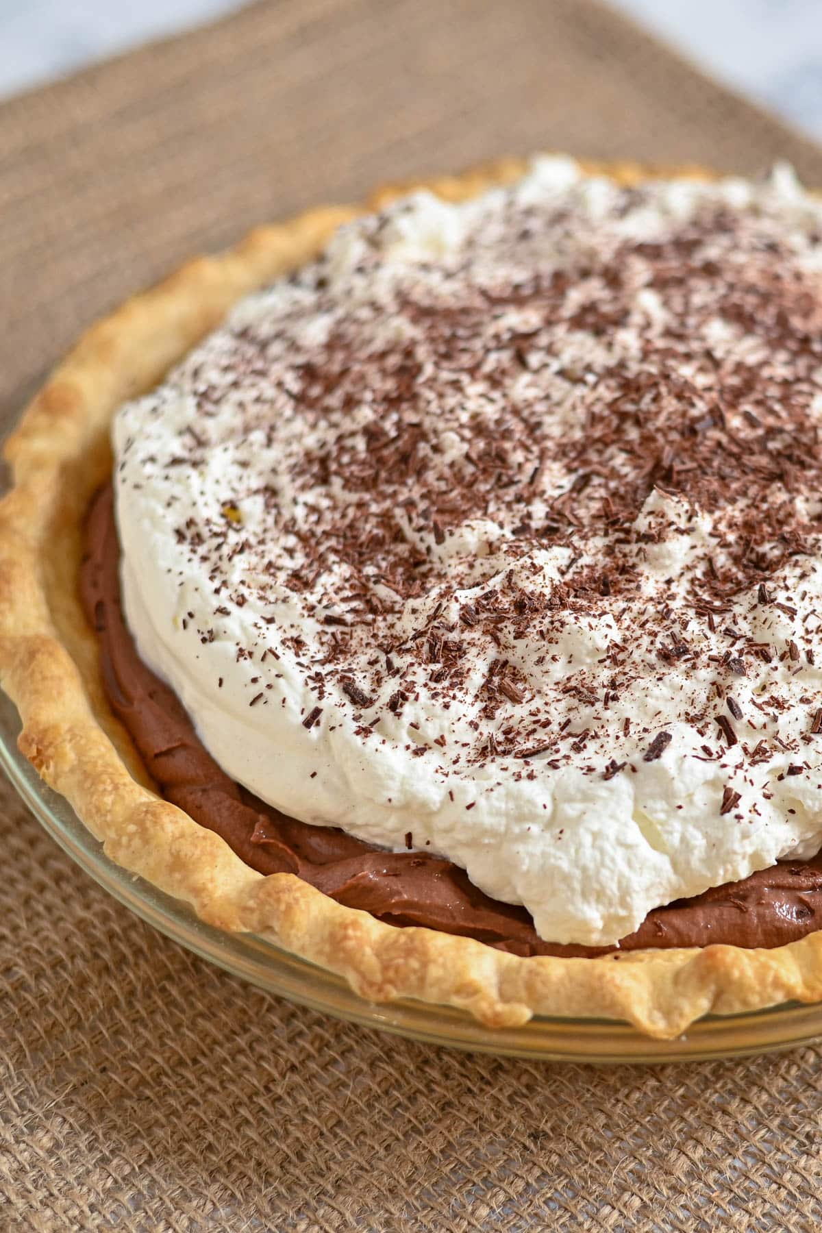 A chocolate cream pie topped with whipped cream and chocolate shavings on a woven placemat.