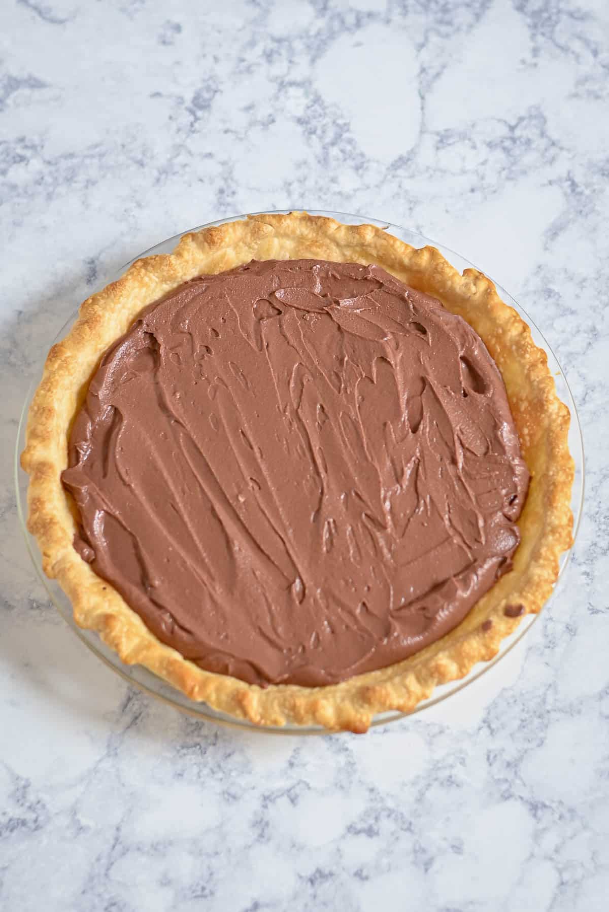 A chocolate cream pie with a golden crust on a marble countertop.