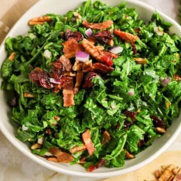 Chopped kale salad with bacon, pecans, dried cranberries, and red onion in a white bowl.