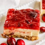 A cheesecake bar with a crumb crust and cranberry topping, garnished with whole cranberries.